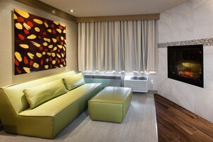 Una sala de estar moderna con un sofá verde, un pequeño reposapiés, una chimenea y un cuadro abstracto grande en la pared.