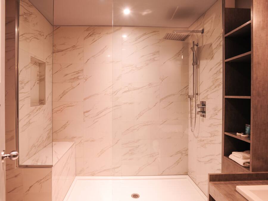 Un baño moderno con ducha acristalada, paredes de mármol y tocador de madera.