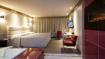 Habitación de hotel moderna con una cama grande, un escritorio, una silla, un televisor y un baño con bañera.