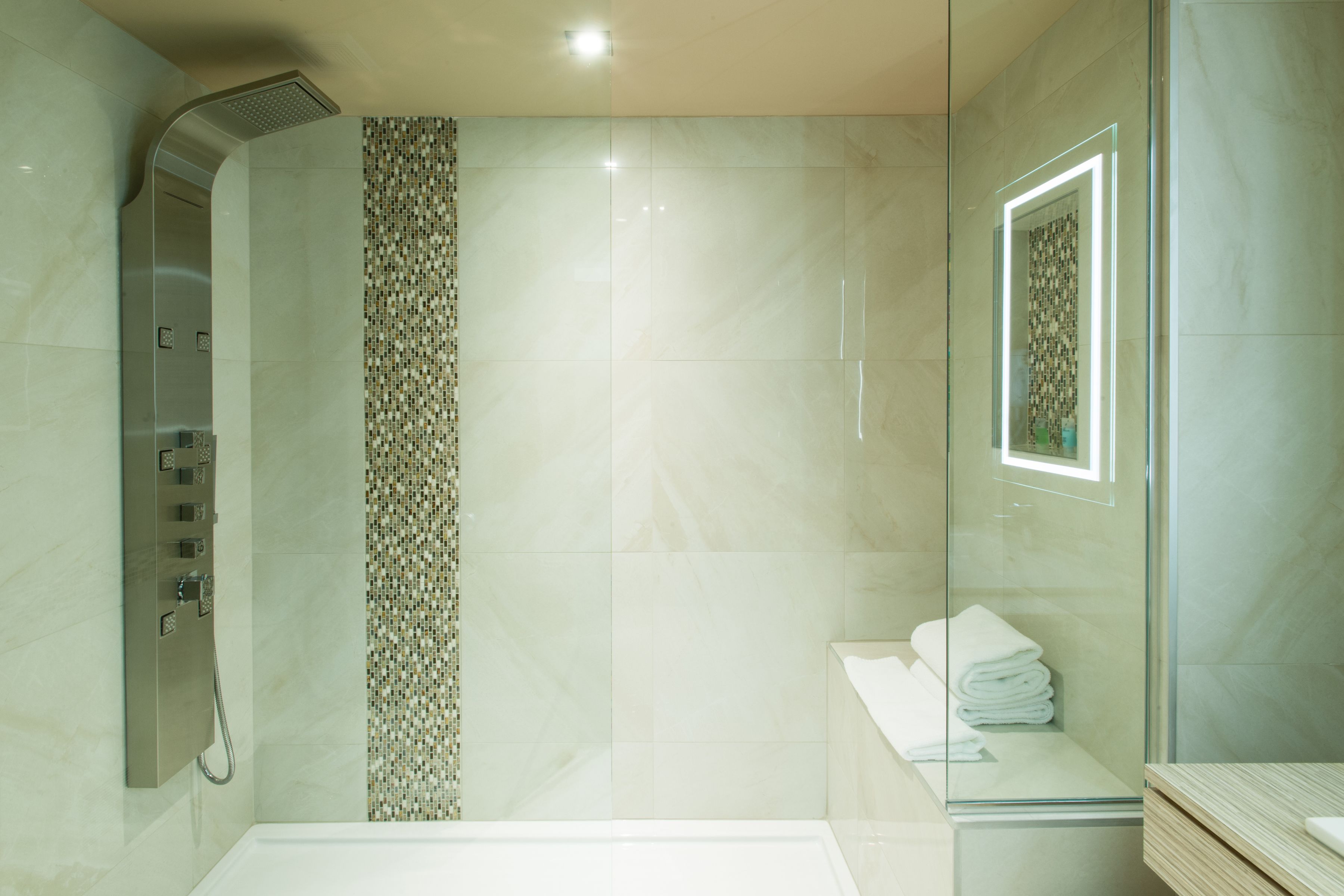 Un baño moderno con cabina de ducha de vidrio, pared de ducha con azulejos y mampara de vidrio que separa la ducha del área del inodoro.