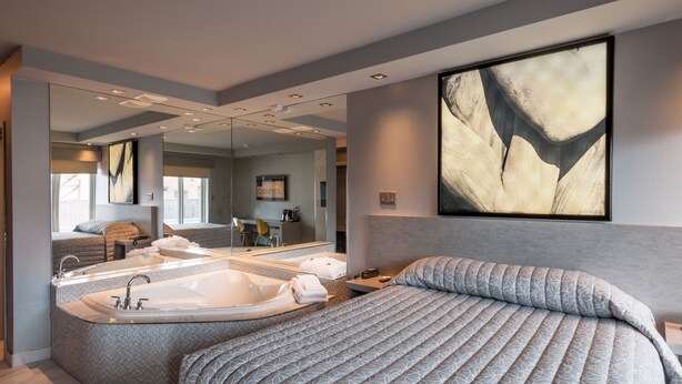 A modern hotel room with a large bed, a separate bathroom with a bathtub, a large mirror, and a painting on the wall. - Le Chabrol Hotel & Suites (Montreal)