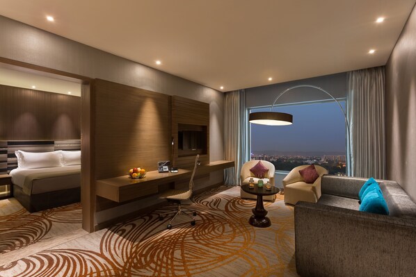 Un hotel moderno con cama, escritorio, sillón, sofá y vista a la ciudad de noche.
