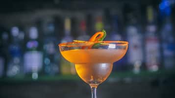A cocktail in a martini glass with a garnish, surrounded by red chili peppers and green herbs on a reflective surface.