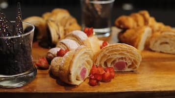 Een houten plank met gebak, waaronder croissants en een chocoladedessert, en een glas donkere vloeistof.