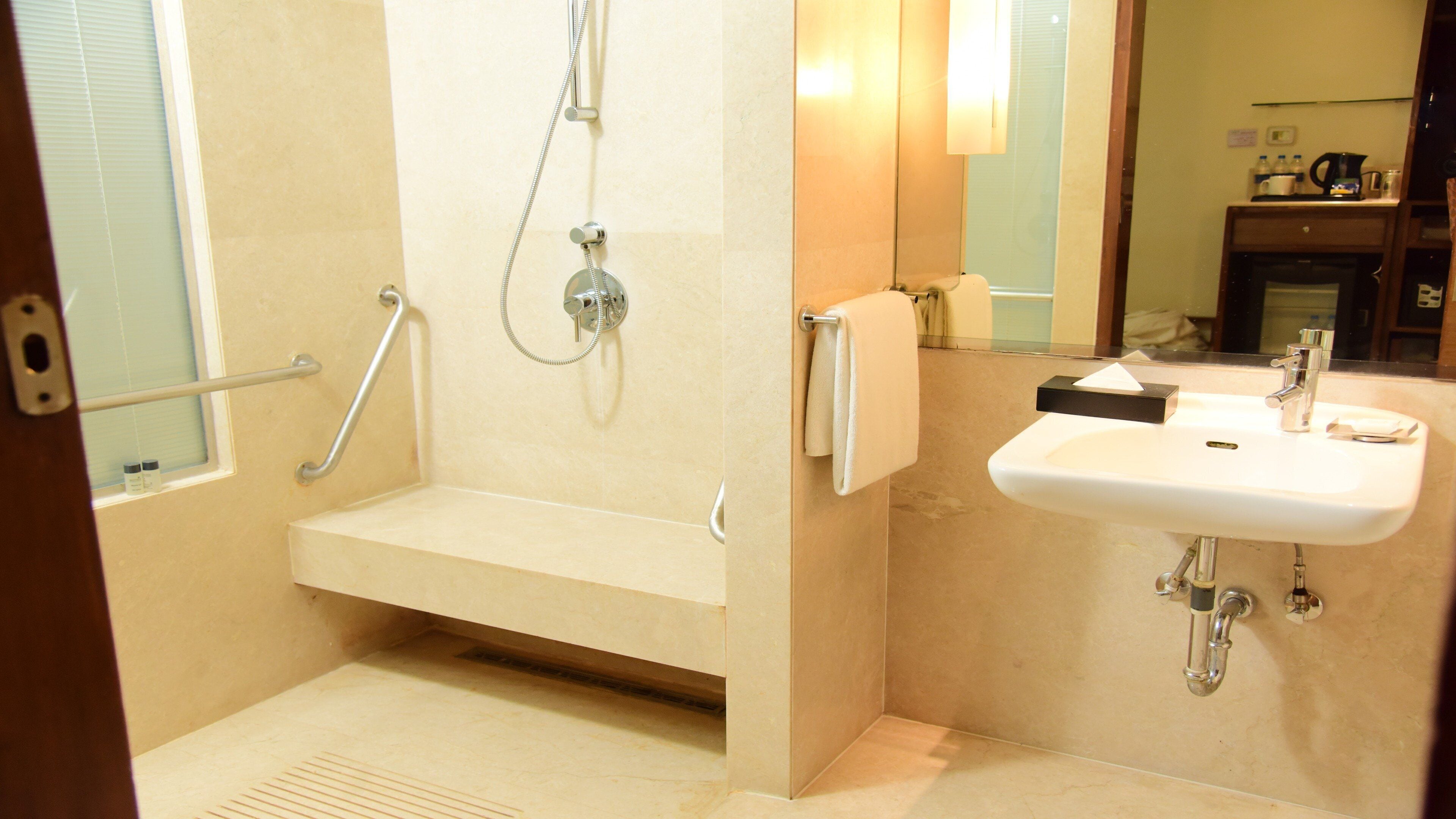 A modern bathroom with a walk-in shower, grab bars, a sink, and a mirror.