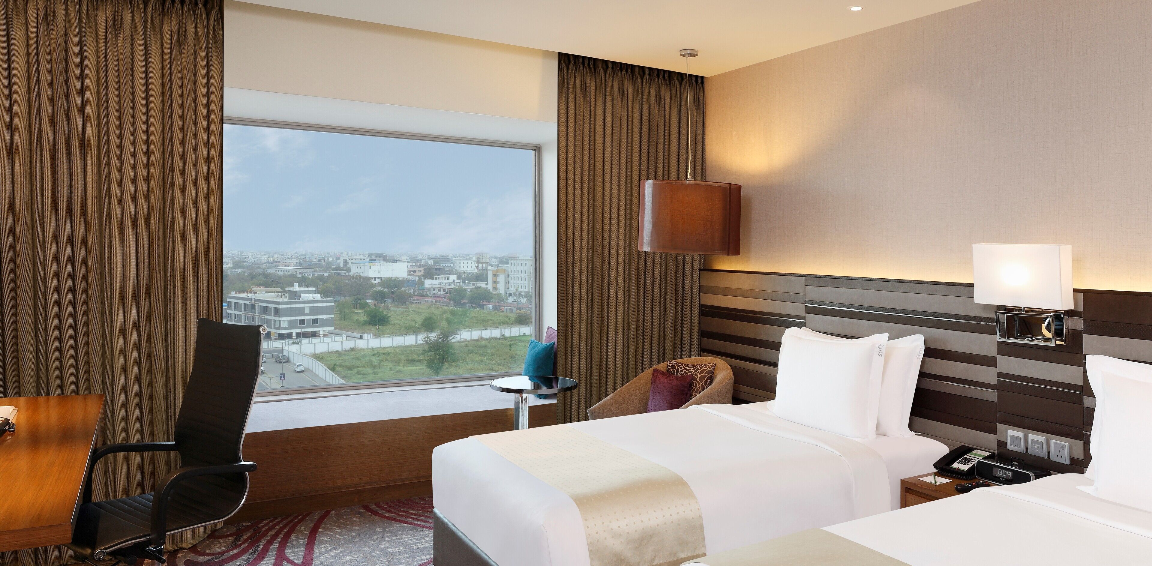 A hotel room with a large window, a bed, a desk, and a chair.