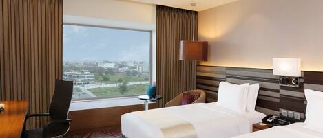 A hotel room with a large window, a bed, a desk, and a chair.