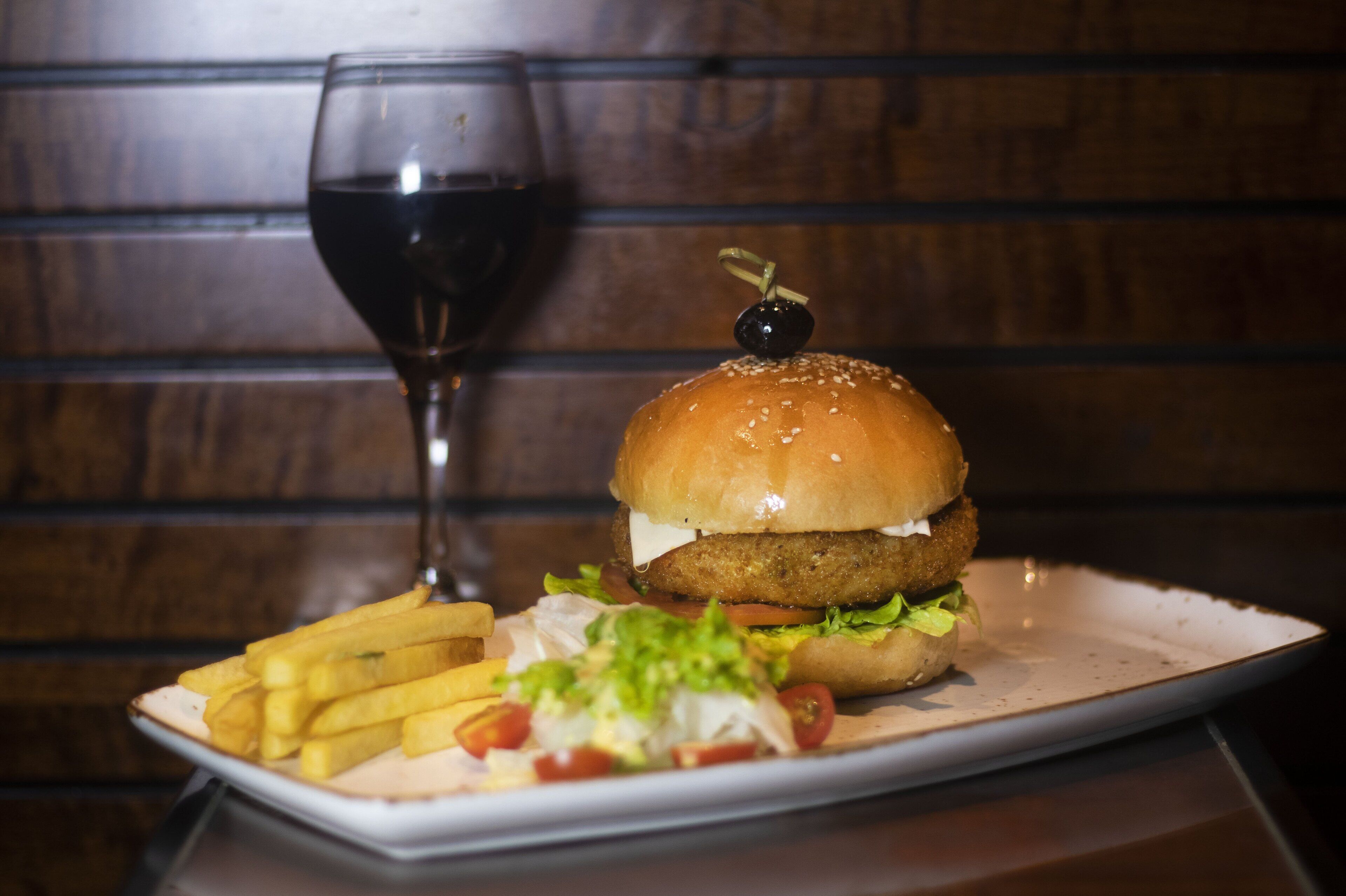 Un plat amb una hamburguesa, patates fregides i un got de vi negre.
