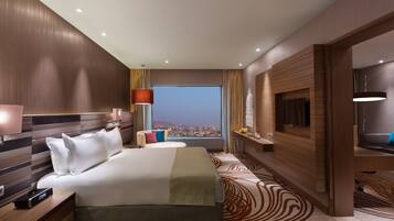 A hotel room with a large bed, a desk, a view of the city, and a modern design.