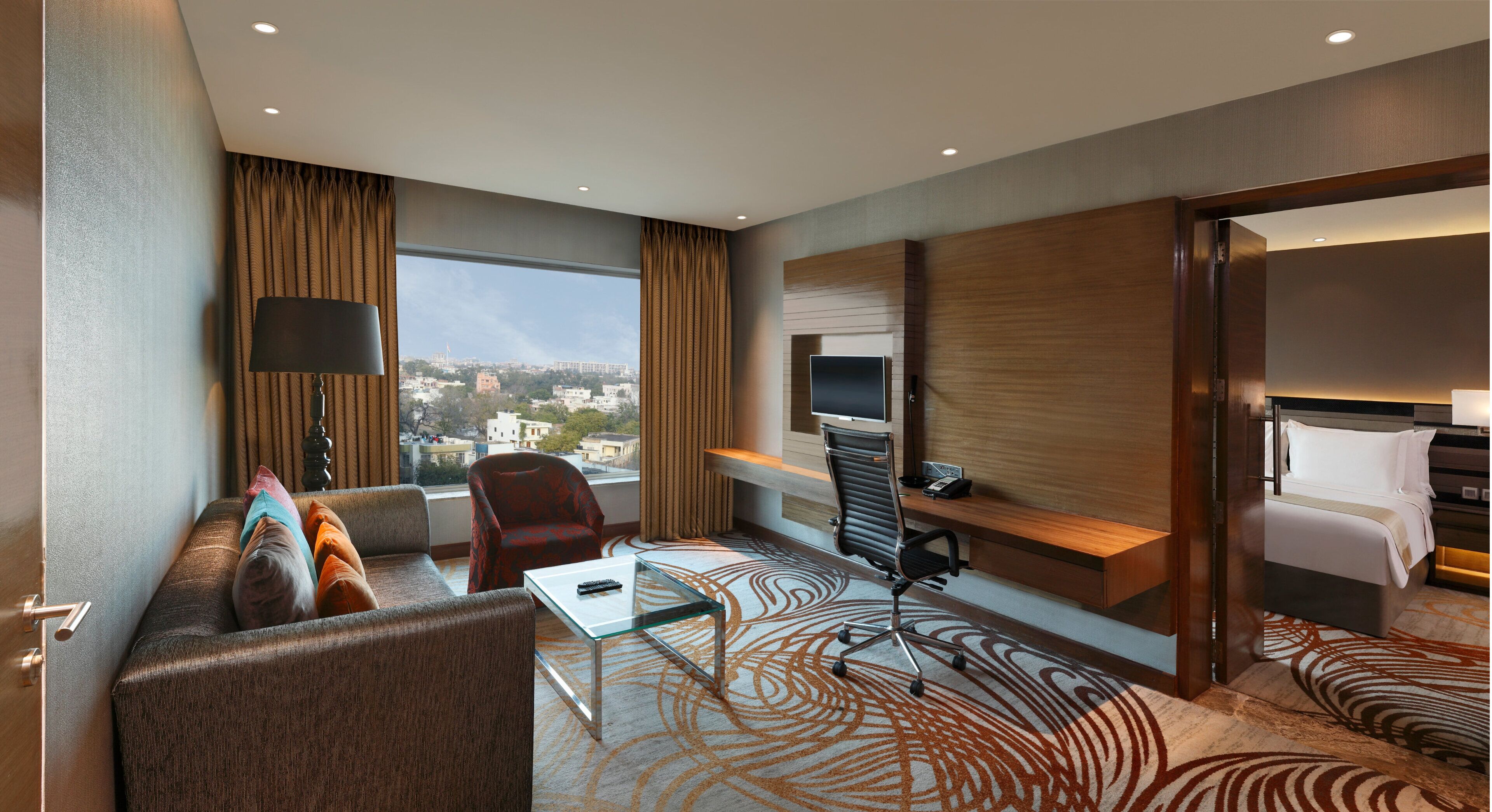 A hotel room with a sofa, a desk, a chair, a TV, and a bed.
