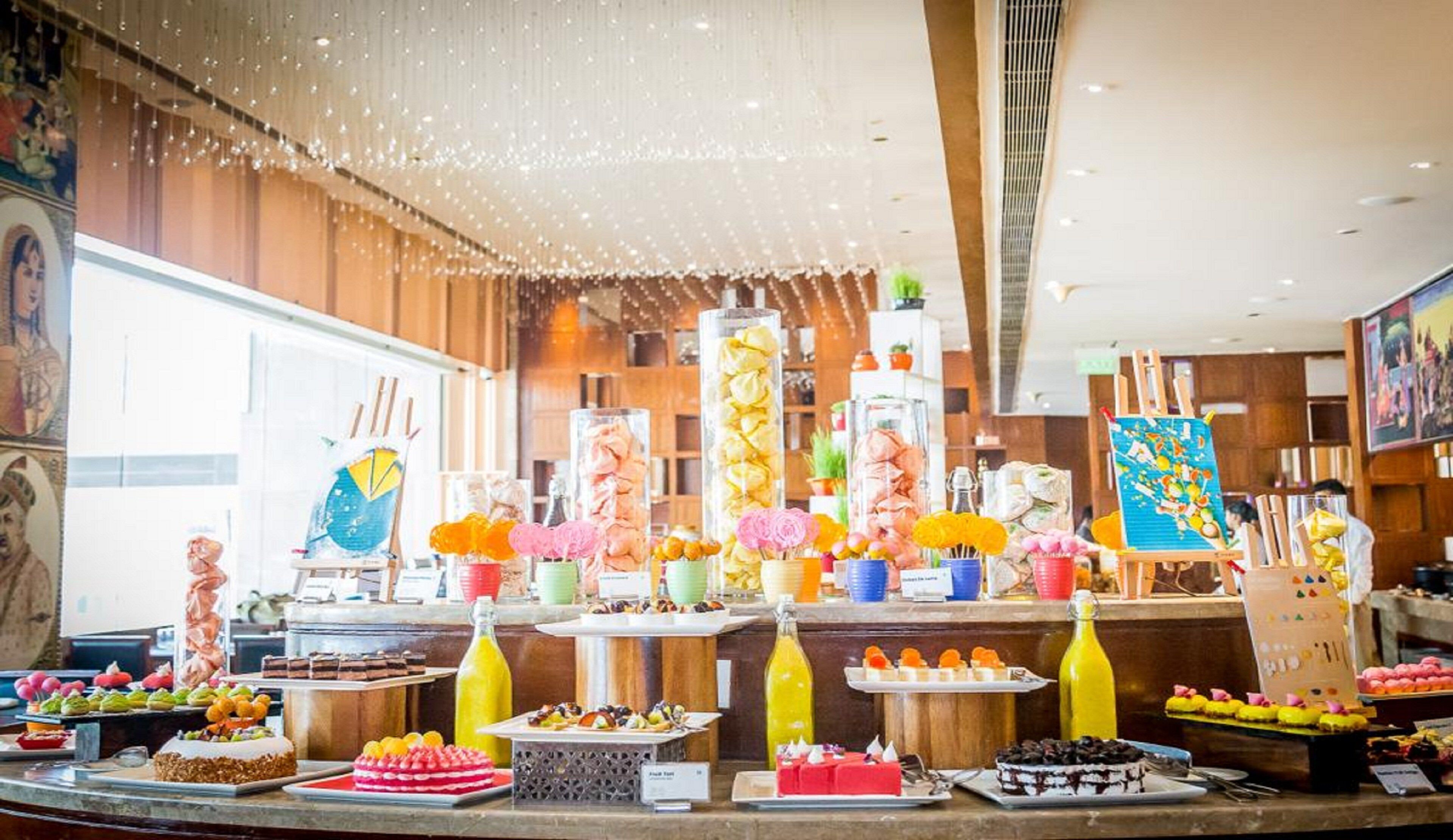 Un bufé con diversos postres y bebidas, entre ellos pasteles, repostería y arreglos de frutas.