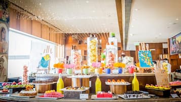 Un bufé con diversos postres y bebidas, entre ellos pasteles, repostería y arreglos de frutas.