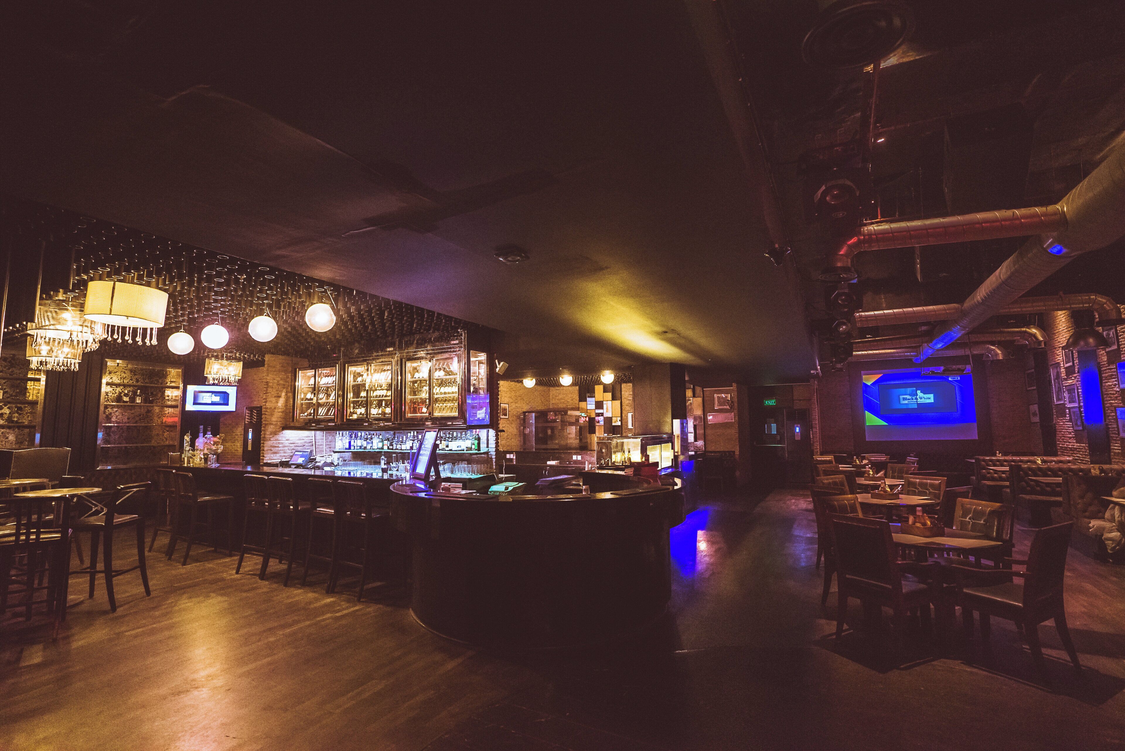 Una zona de bar con mostrador, taburetes y una pantalla de proyección.