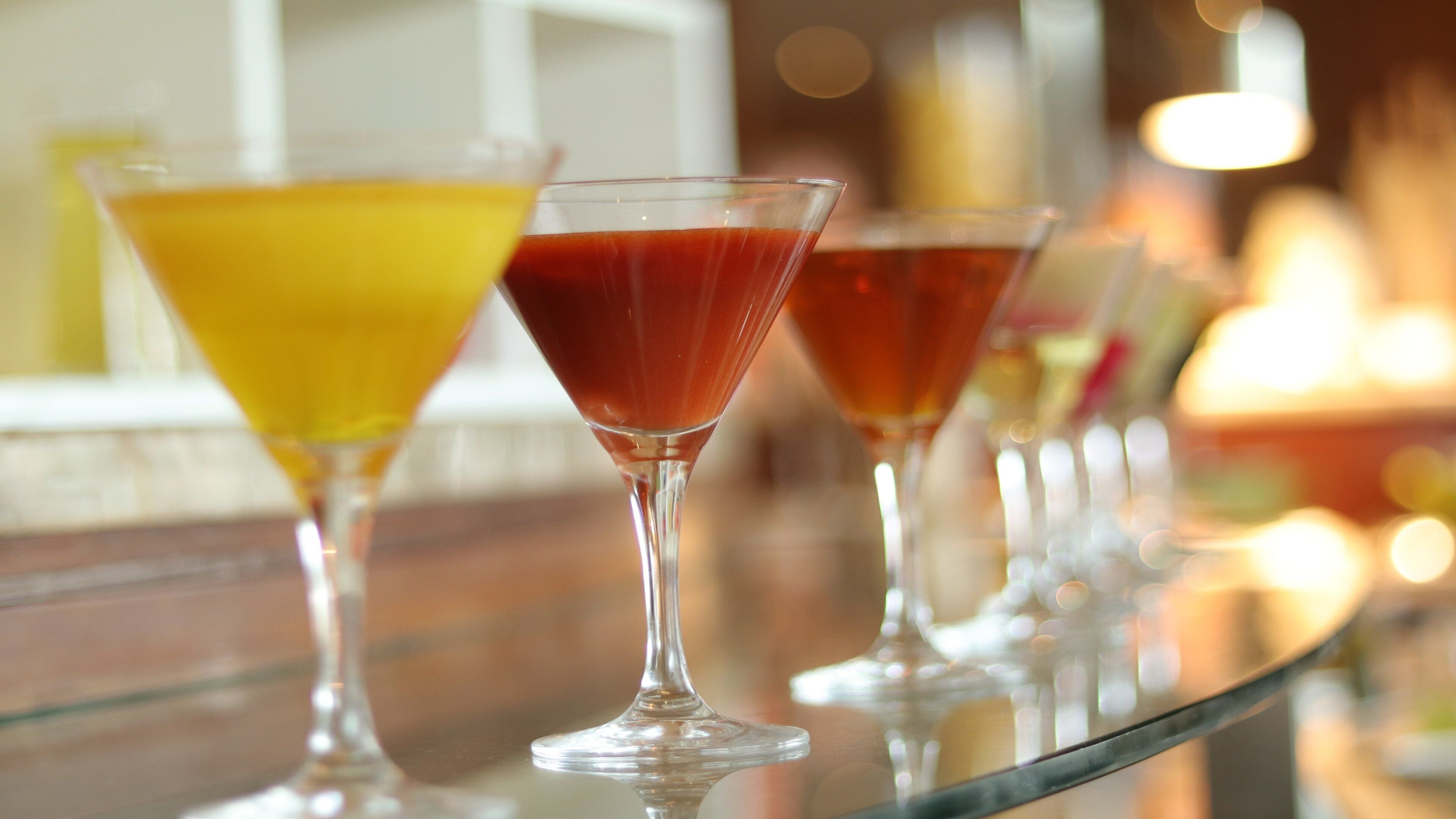 A bar with a row of martini glasses filled with different colored drinks.