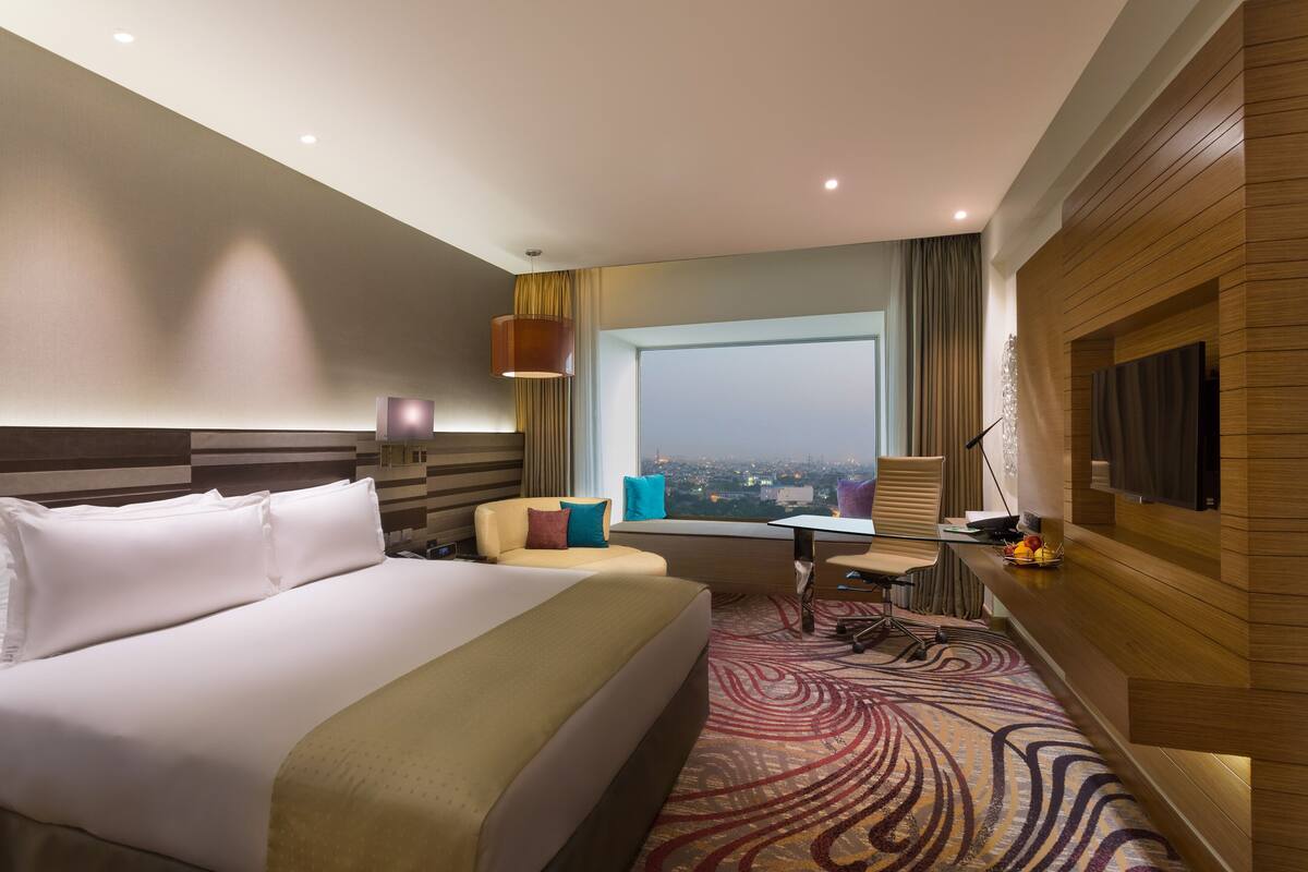 Ein Hotelzimmer mit einem großen Bett, einem Schreibtisch, einem Stuhl und Blick auf die Stadt.