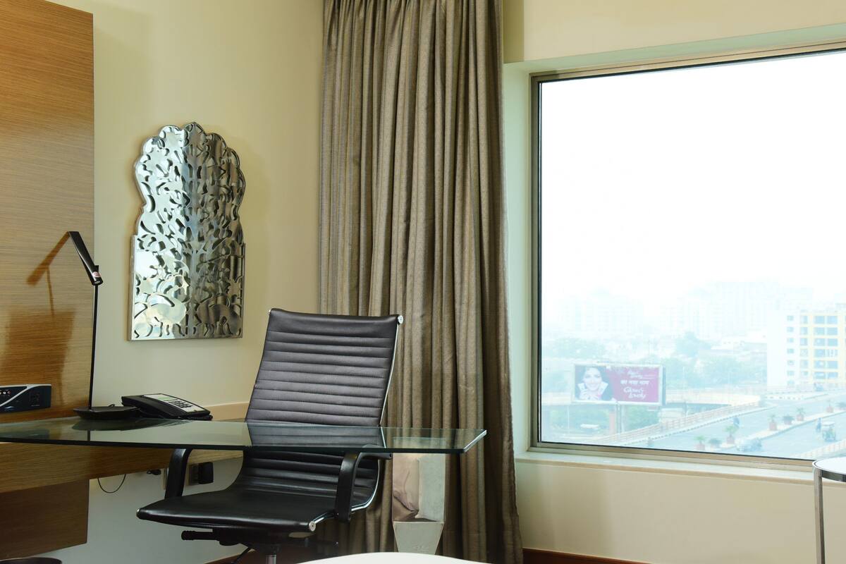Ein Hotelzimmer mit modernem Schreibtisch, schwarzem Bürostuhl, Wanddeko und einem großen Fenster mit Blick auf die Stadt.