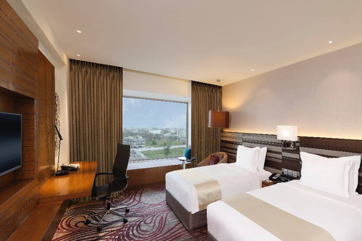 Ein Hotelzimmer mit zwei Betten, einem Fernseher, einem Schreibtisch und Blick auf die Stadt.