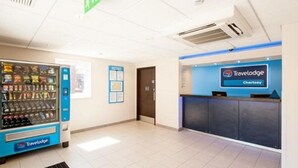 A Travelodge reception area with a vending machine, a reception desk, and a door. - Travelodge Chertsey (Chertsey)