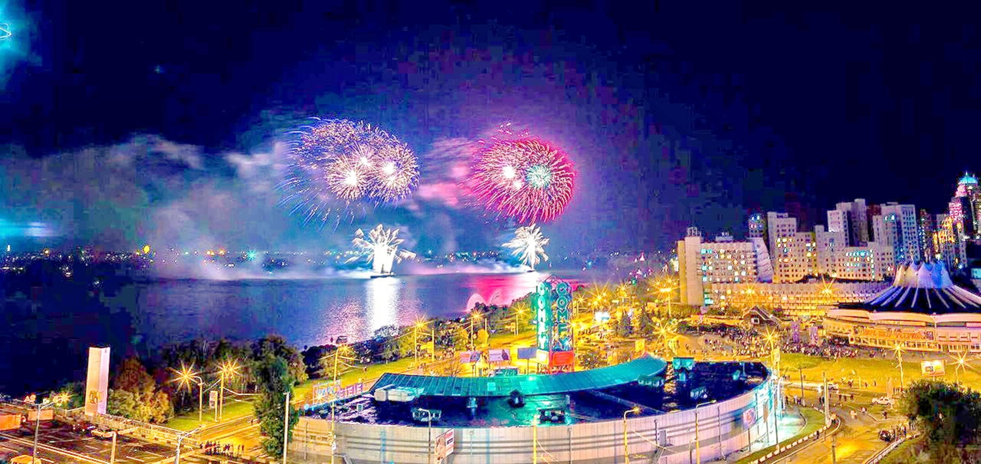 Une vue sur le front de mer illuminée par des feux d’artifice, un grand bâtiment circulaire et un paysage urbain en arrière-plan.