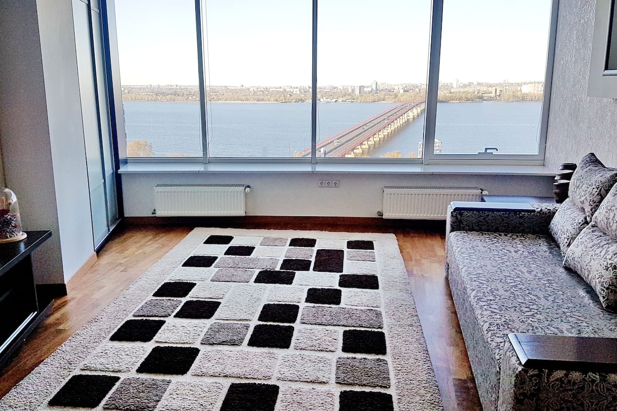 A living room with a large window, a patterned rug, a sofa, and a small table.
