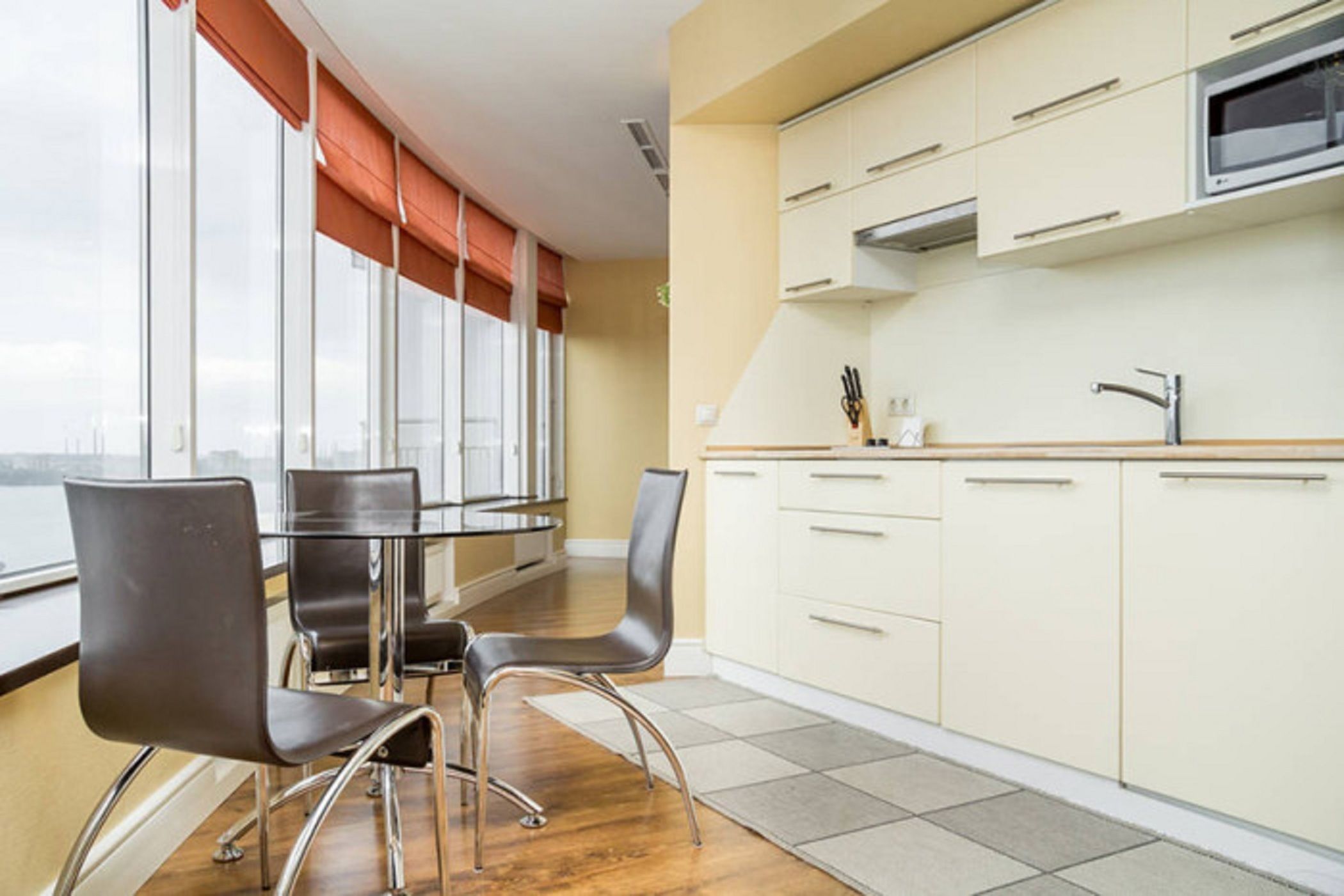 A modern kitchen with a view of the city, a dining area with chairs, and a large window with orange blinds.