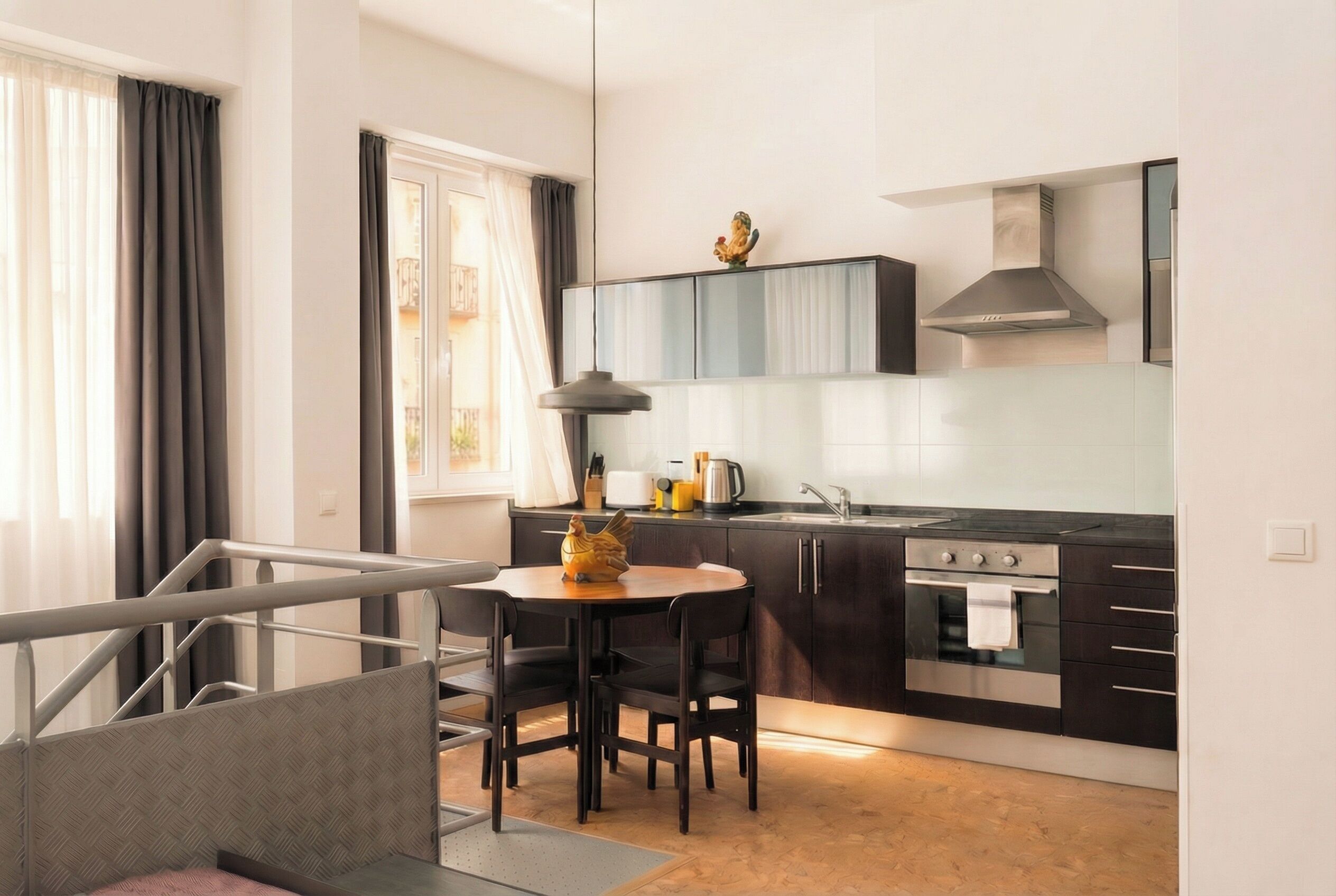 A modern kitchen with dark cabinetry, a stainless steel stove, and a dining area with a table and chairs.