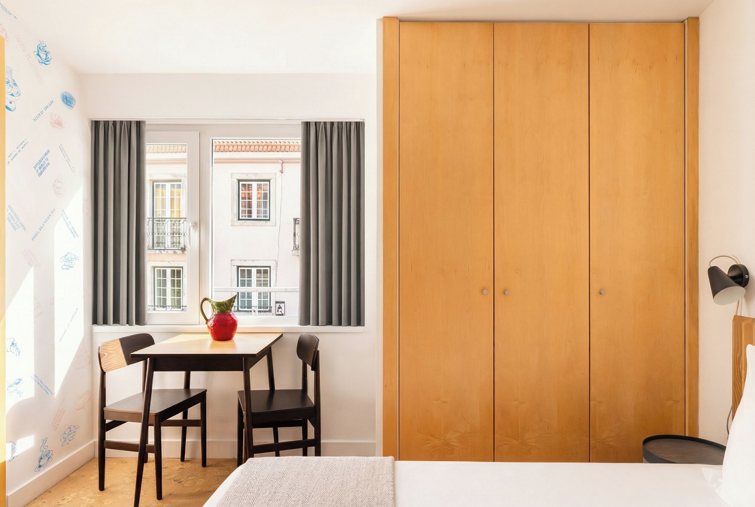 Une pièce comprenant un lit, une armoire en bois, une table avec des chaises, une fenêtre avec des rideaux et une lampe.