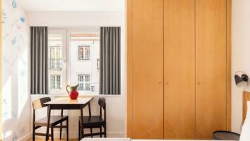 Une pièce comprenant un lit, une armoire en bois, une table avec des chaises, une fenêtre avec des rideaux et une lampe.