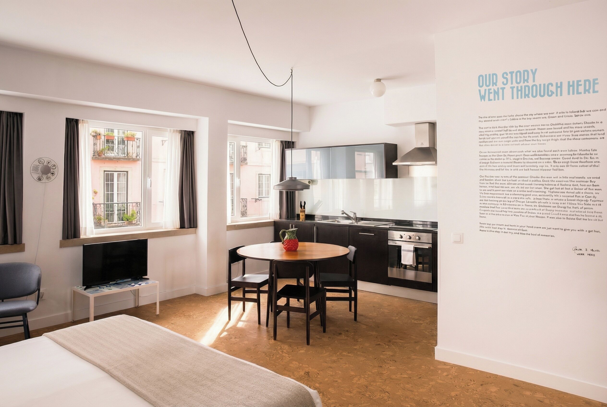 A modern hotel room with a bed, a TV, a dining table, and a kitchen area.