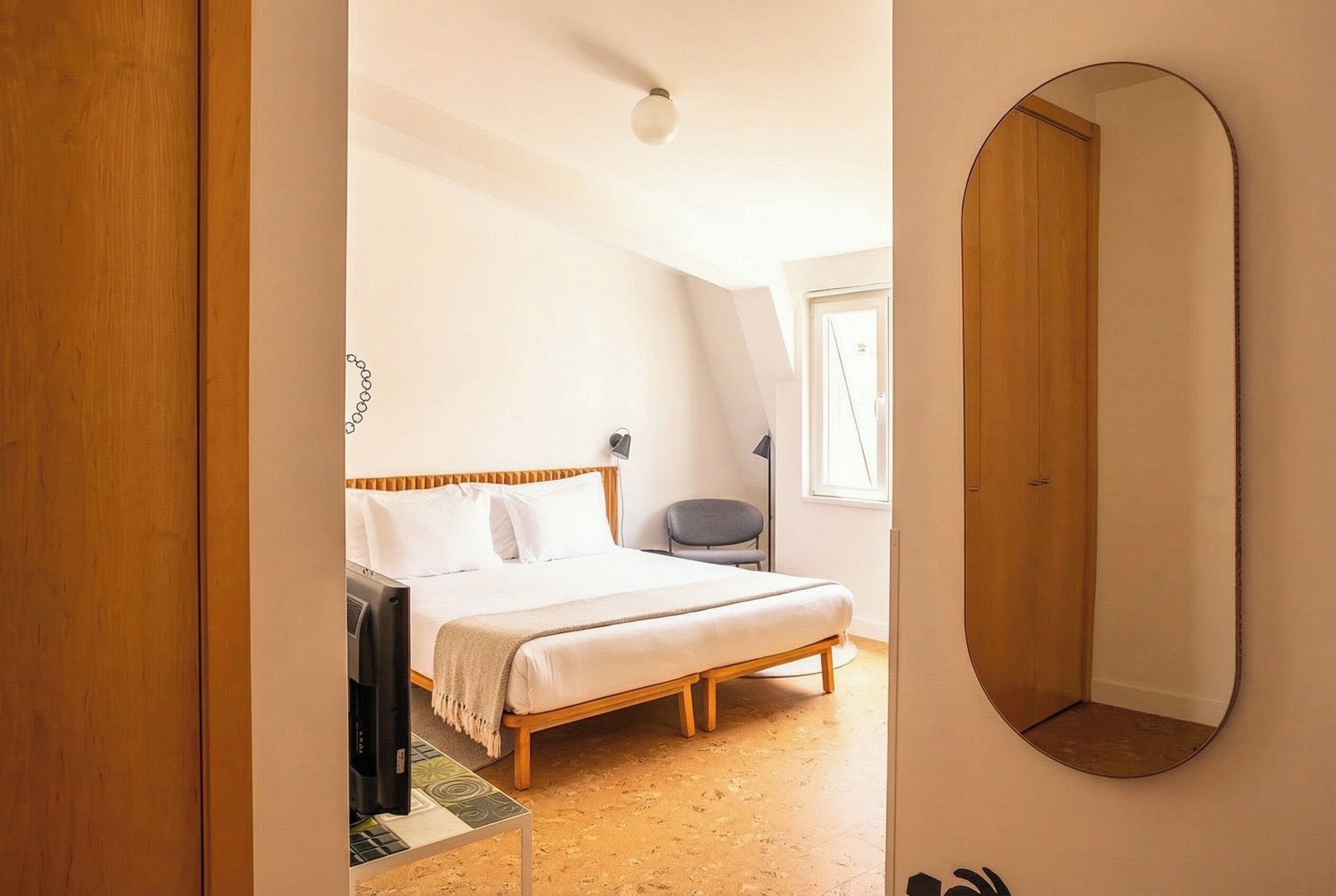 A bedroom with a bed, a chair, a desk, a mirror, and a wardrobe.