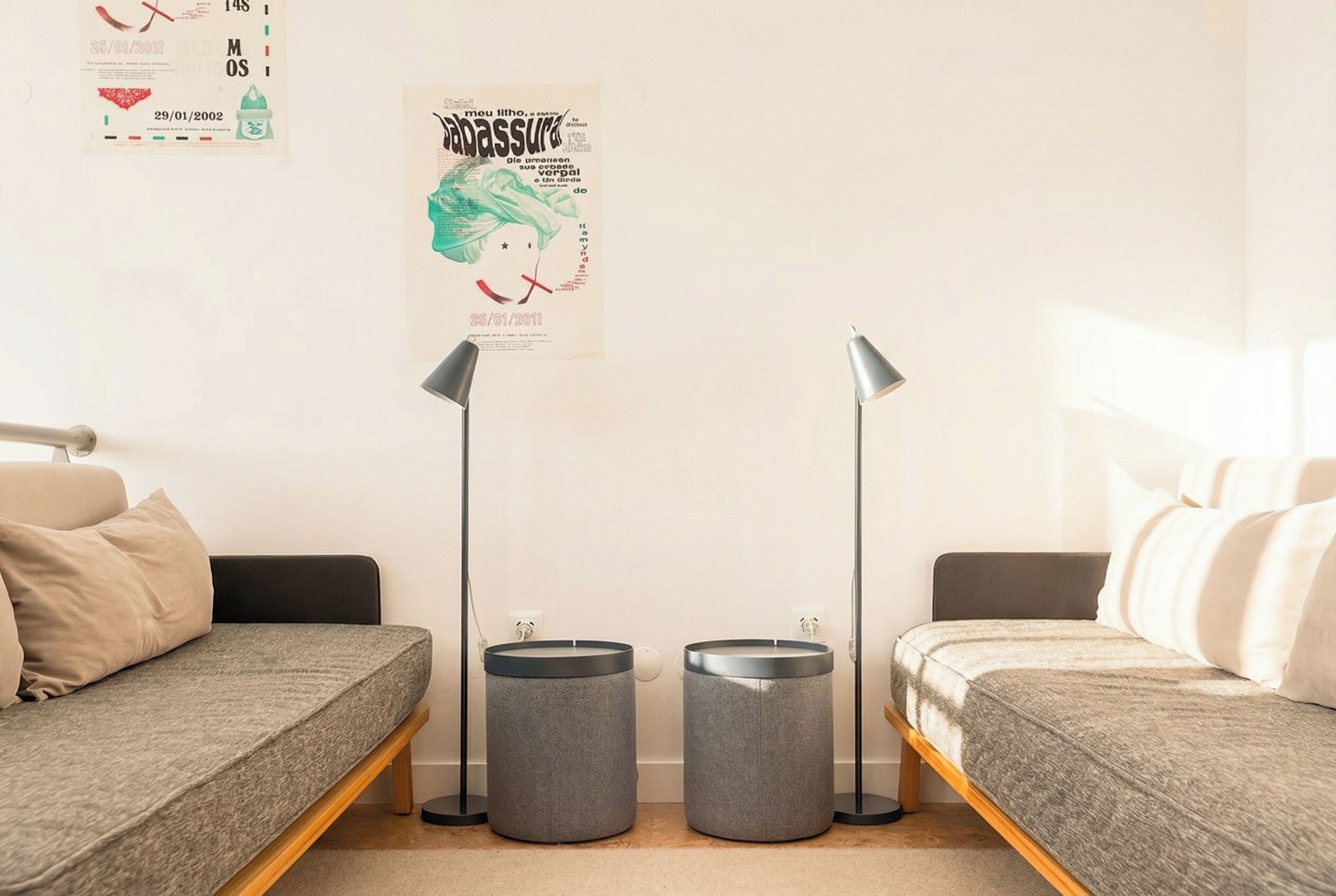 A minimalist room with two single beds, grey cushions, and two grey trash bins.