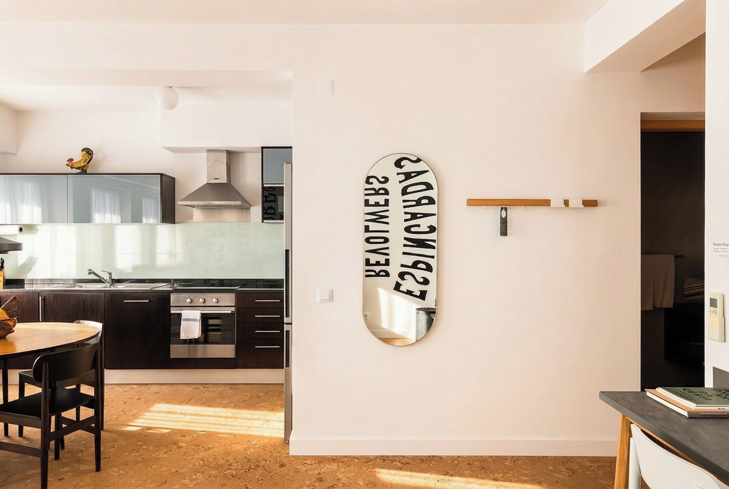 Una cocina moderna con armarios oscuros, un horno de acero inoxidable y un comedor con mesa y sillas de madera.