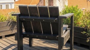 A wooden deck with a bench, overlooking a cityscape with buildings and greenery.