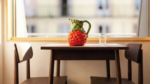 A table with a pitcher and a glass, two chairs, and a window with a view of buildings.