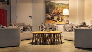 A modern living room with a round wooden table, two grey sofas, and a painting of a rural scene on the wall.