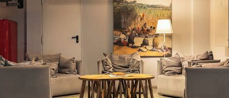 A modern living room with a round wooden table, two grey sofas, and a painting of a rural scene on the wall.
