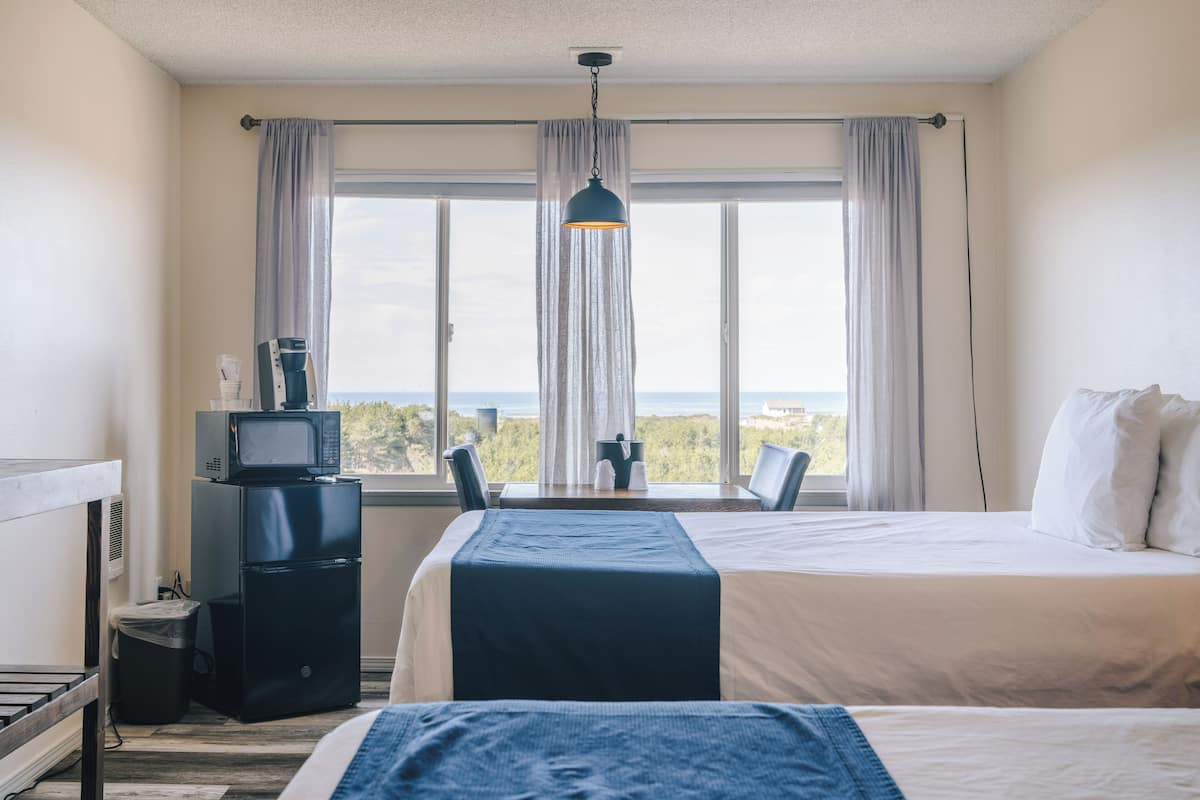 A hotel room with a bed, a desk with a computer, a microwave, and a trash bin.