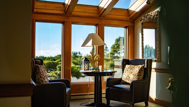 Una habitación con dos sillones de cuero, una mesita redonda con lámpara y vistas a zonas verdes a través de amplias ventanas.