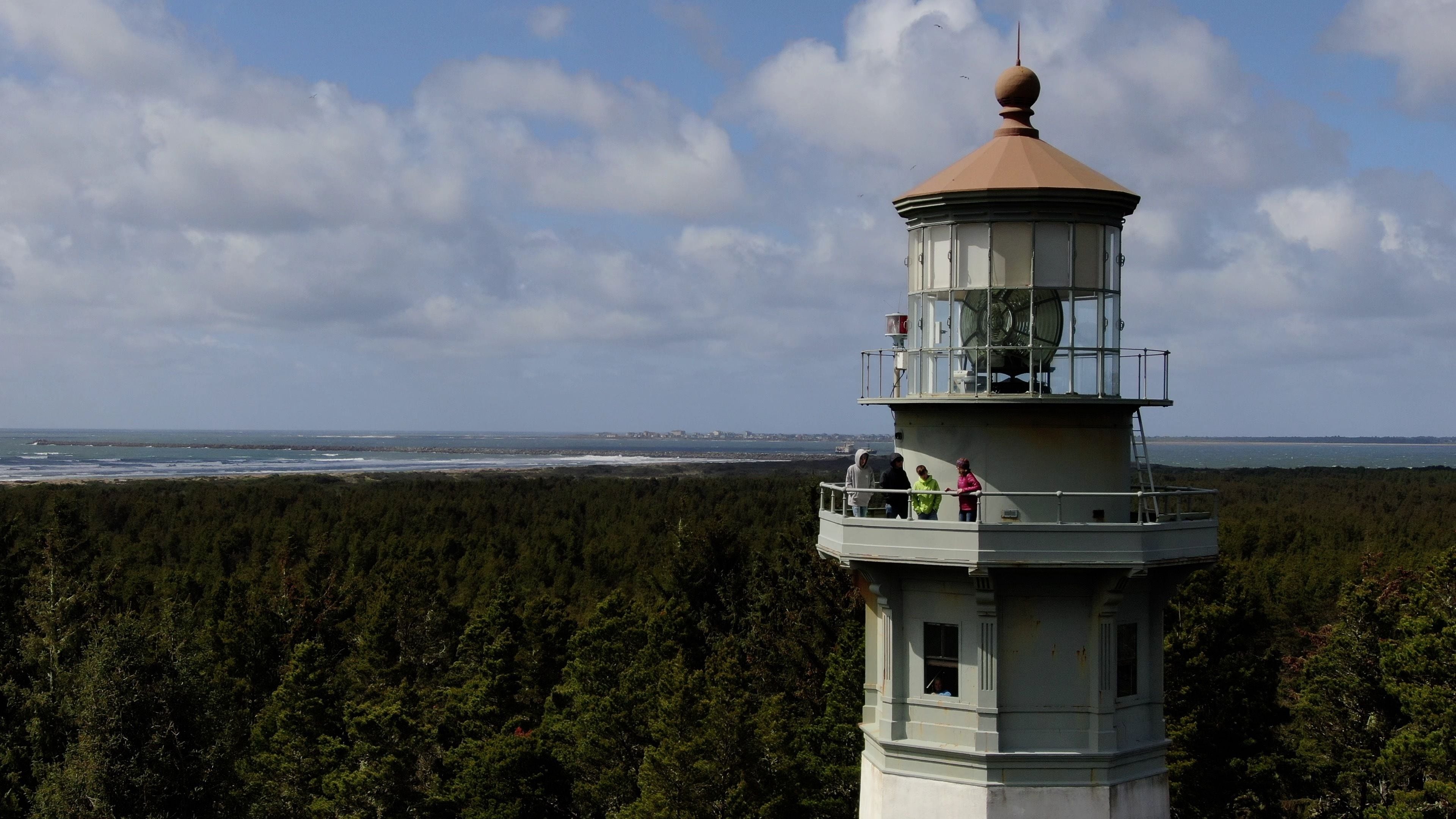 Ein Leuchtturm mit freiem Blick auf den Ozean und einer bewaldeten Landschaft im Hintergrund.
