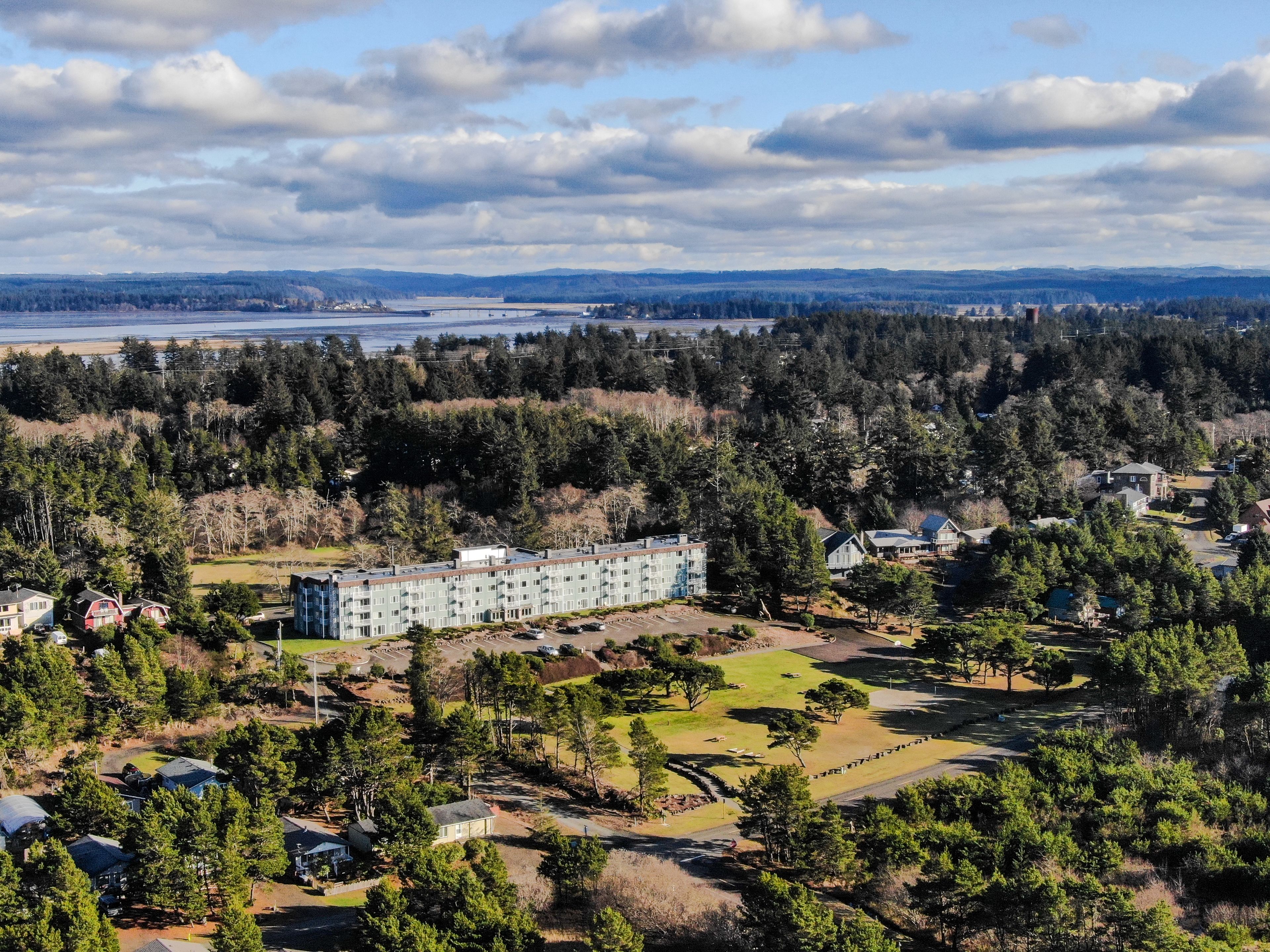 Um edifício grande com vários andares, rodeado por uma floresta densa e um campo de golfe.