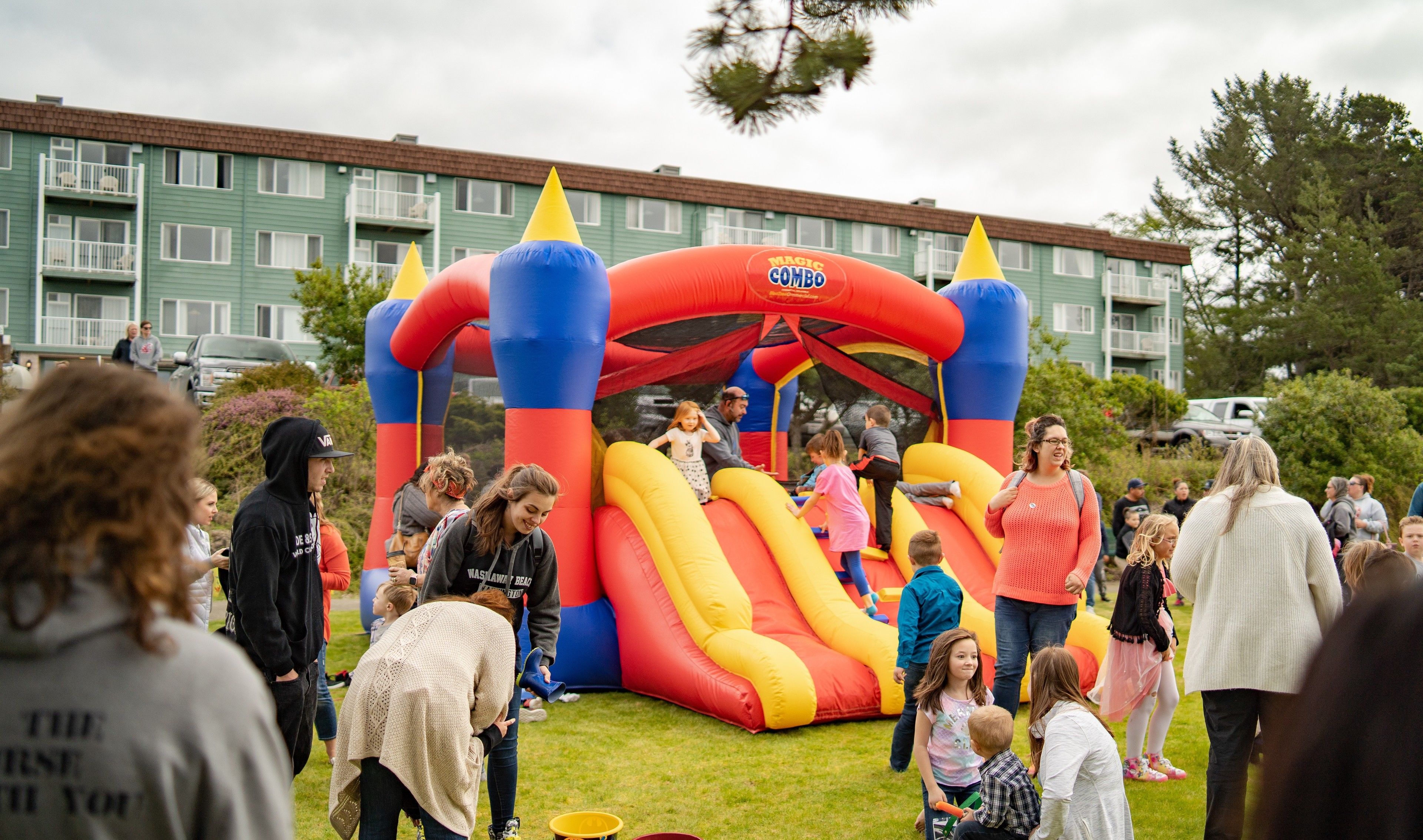 A colorful inflatable bounce house with a slide, surrounded by people, in front of a residential building.