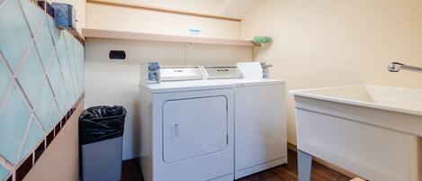 A laundry area with a washing machine, a sink, and a trash bin.