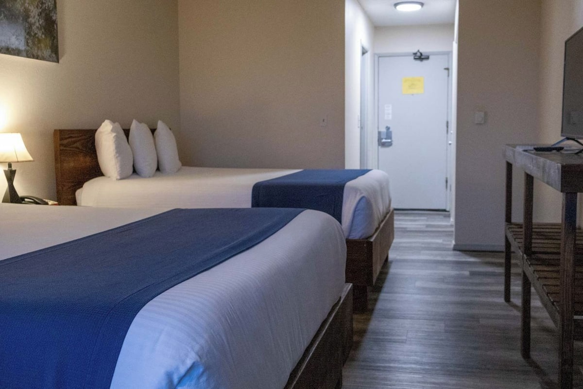 A hotel room with two beds, a television on a wooden table, and a hallway leading to a door.