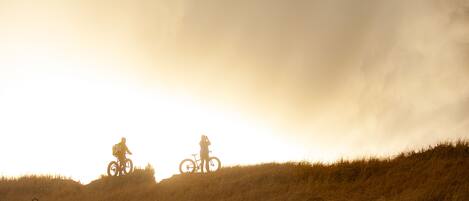 A silhouette of a person on a bicycle on a grassy hill with a cloudy sky.
