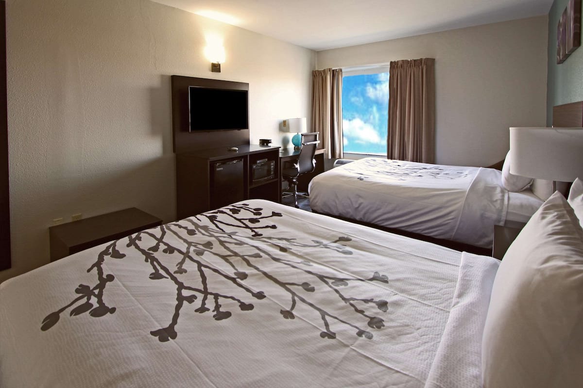 Habitación de hotel con dos camas, televisión, escritorio y ventana con cortinas.