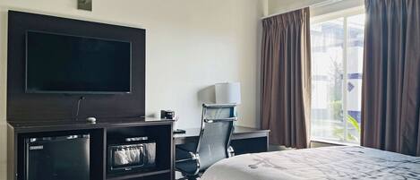 A hotel room with a bed, a desk, a chair, a television, and a window with curtains.