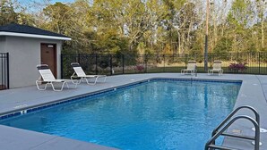 A rectangular swimming pool with a metal ladder, surrounded by a black metal fence. There are two lounge chairs and a small building with a door. - Sleep Inn & Suites Foley - Gulf Shores North (Foley)