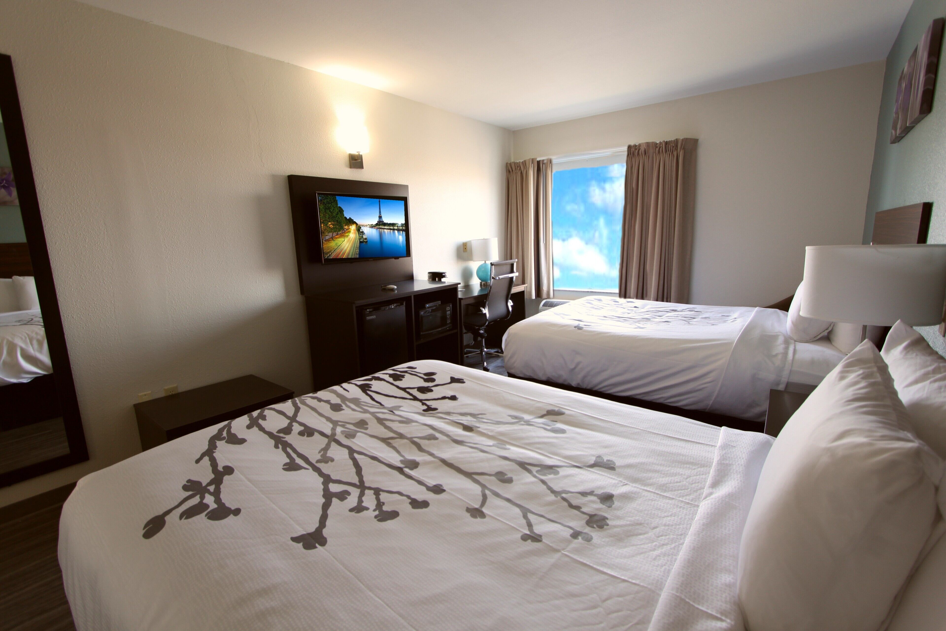 Een hotelkamer met twee bedden, een televisie, een bureau en een raam met gordijnen.