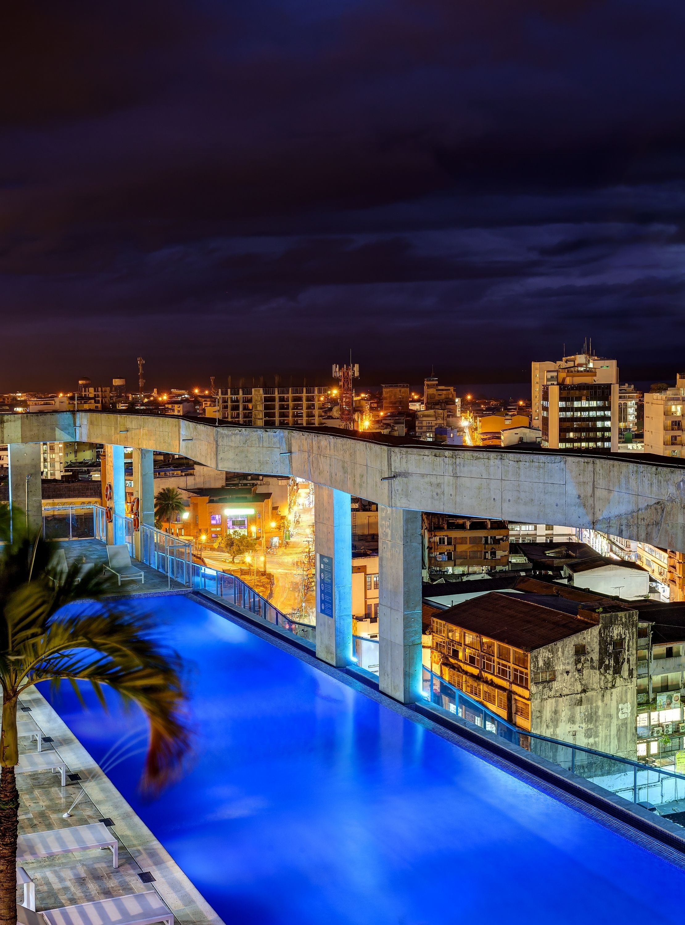 Vista nocturna de una piscina con un paisaje urbano al fondo.