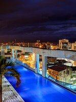 Vista nocturna de una piscina con un paisaje urbano al fondo.